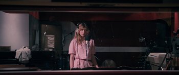 Movie still from “The Look of Love” (2013), directed by Michael Winterbottom – A girl in a pink dress is recording a song; Medium shot, Low angle