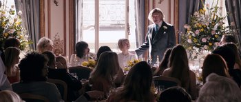Movie still from “The Look of Love” (2013), directed by Michael Winterbottom – A group of people sitting around a table; Medium shot, Over the shoulder angle
