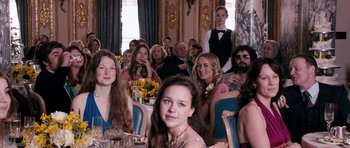 Movie still from “The Look of Love” (2013), directed by Michael Winterbottom – A group of people sitting around a table; Medium shot, Over the shoulder angle