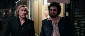 Movie still from “The Look of Love” (2013), directed by Michael Winterbottom – A man and a woman wearing sunglasses and a suit; Medium shot, Over the shoulder angle