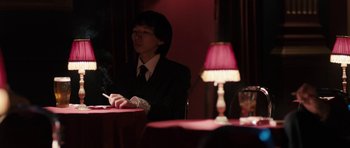 Movie still from “The Look of Love” (2013), directed by Michael Winterbottom – A man sitting at a table with a cigarette in his mouth; Medium shot, Over the shoulder angle