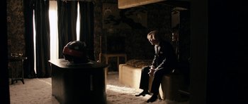 Movie still from “The Look of Love” (2013), directed by Michael Winterbottom – A man sitting on a chair in a dark room; Wide shot, Over the shoulder angle