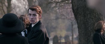 Movie still from “The Look of Love” (2013), directed by Michael Winterbottom – A young man in a black jacket is standing in a wooded area; Close Up shot, Over the shoulder angle