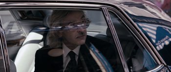 Movie still from “The Look of Love” (2013), directed by Michael Winterbottom – A man in a suit sitting in the back seat of a car; Close Up shot, Over the shoulder angle
