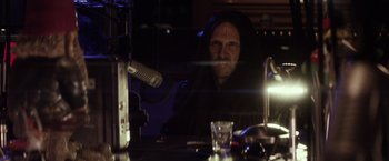 Movie still from “The Lords of Salem” (2012), directed by Rob Zombie – A man in a black robe sitting in front of a microphone; Close Up shot, Over the shoulder angle