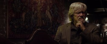 Movie still from “The Lords of Salem” (2012), directed by Rob Zombie – A man sitting in a chair in front of a painting; Close Up shot, Over the shoulder angle