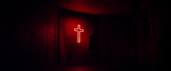 Movie still from “The Lords of Salem” (2012), directed by Rob Zombie – A woman standing in front of a neon cross sign; Extreme Wide shot, Low angle