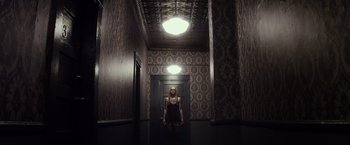 Movie still from “The Lords of Salem” (2012), directed by Rob Zombie – A woman standing in a dark room in front of a door; Wide shot, Low angle