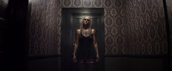 Movie still from “The Lords of Salem” (2012), directed by Rob Zombie – A woman standing in front of a door wearing tattoos; Medium shot, Overhead angle