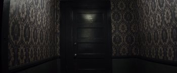 Movie still from “The Lords of Salem” (2012), directed by Rob Zombie – A black door in a room with a pattern wall paper; Wide shot, Overhead angle