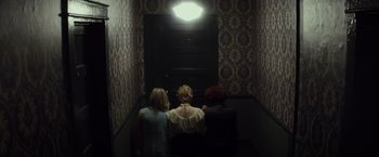 Movie still from “The Lords of Salem” (2012), directed by Rob Zombie – Three people are sitting in a dark hallway; Wide shot, Overhead angle