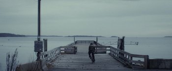Movie still from “The Lords of Salem” (2012), directed by Rob Zombie – A person riding a bike on a wooden pier; Extreme Wide shot, High angle