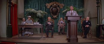 Movie still from “The Lost World” (1960), directed by Irwin Allen – A group of people sitting at a podium in front of a microphone; Wide shot, Low angle