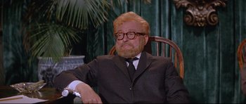 Movie still from “The Lost World” (1960), directed by Irwin Allen – An older man sitting in a chair wearing a suit; Medium shot, Low angle
