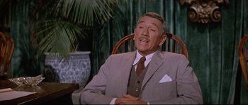 Movie still from “The Lost World” (1960), directed by Irwin Allen – An older man wearing a suit and tie sitting in a chair; Medium shot, Low angle