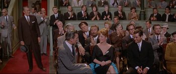 Movie still from “The Lost World” (1960), directed by Irwin Allen – A group of people sitting in chairs in front of a crowd; Wide shot, Over the shoulder angle