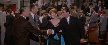 Movie still from “The Lost World” (1960), directed by Irwin Allen – Two men and a woman shaking hands in a crowd of onlookers; Medium shot, Over the shoulder angle