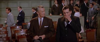 Movie still from “The Lost World” (1960), directed by Irwin Allen – Two men in suits stand in front of a crowd; Medium shot, Over the shoulder angle