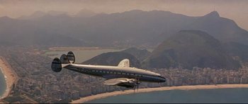 Movie still from “The Lost World” (1960), directed by Irwin Allen – An airplane is flying over a city and a body of water; Extreme Wide shot, Low angle