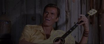 Movie still from “The Lost World” (1960), directed by Irwin Allen – A man in a yellow shirt is holding a guitar; Close Up shot, Low angle