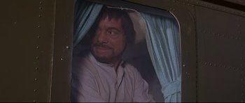 Movie still from “The Lost World” (1960), directed by Irwin Allen – A man with a beard and a cowboy hat is looking out a window; Close Up shot, Over the shoulder angle