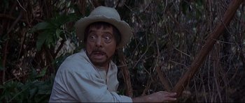 Movie still from “The Lost World” (1960), directed by Irwin Allen – A man in a hat and a white shirt is in the woods; Close Up shot, High angle