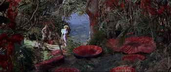 Movie still from “The Lost World” (1960), directed by Irwin Allen – A woman standing next to a tree near a body of water; Wide shot, High angle