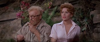 Movie still from “The Lost World” (1960), directed by Irwin Allen – An older man and a younger woman sitting next to each other; Medium shot, Low angle
