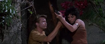 Movie still from “The Lost World” (1960), directed by Irwin Allen – A man and a woman holding guns in a forest; Medium shot, High angle
