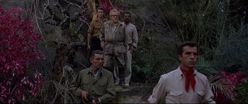 Movie still from “The Lost World” (1960), directed by Irwin Allen – A group of men standing on top of a lush green hillside; Wide shot, Over the shoulder angle