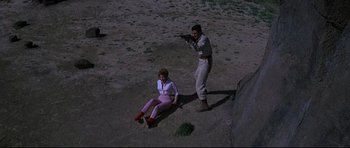 Movie still from “The Lost World” (1960), directed by Irwin Allen – A man and a woman sitting on the ground with a gun in their hands; Wide shot, High angle