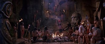 Movie still from “The Lost World” (1960), directed by Irwin Allen – A group of people sitting around a fire pit; Wide shot, High angle