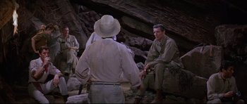 Movie still from “The Lost World” (1960), directed by Irwin Allen – A man sitting on the ground next to another man; Wide shot, High angle
