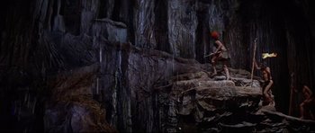 Movie still from “The Lost World” (1960), directed by Irwin Allen – A man with a red hat is climbing a rock wall; Extreme Wide shot, High angle