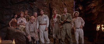 Movie still from “The Lost World” (1960), directed by Irwin Allen – A group of men standing next to each other in a cave; Wide shot, High angle