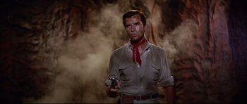 Movie still from “The Lost World” (1960), directed by Irwin Allen – A man holding a cell phone while standing next to a wall; Medium shot, Low angle