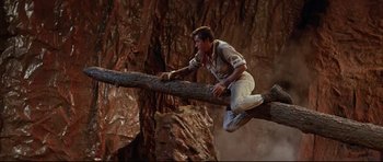 Movie still from “The Lost World” (1960), directed by Irwin Allen – A man climbing a tree branch in the middle of a cave; Wide shot, Low angle