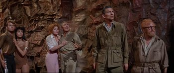 Movie still from “The Lost World” (1960), directed by Irwin Allen – A group of people standing next to each other in front of rocks; Medium shot, Low angle