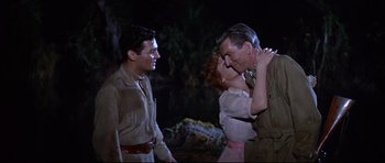 Movie still from “The Lost World” (1960), directed by Irwin Allen – A man and a woman kissing in front of two other men; Medium shot, Over the shoulder angle