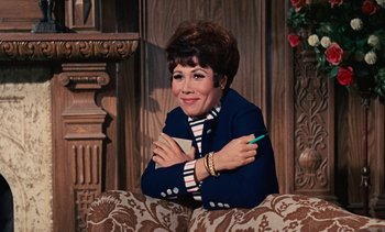 Movie still from “The Love Bug” (1969), directed by Robert Stevenson – An older woman sitting on top of a couch with her arms crossed; Medium shot, High angle