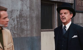 Movie still from “The Love Bug” (1969), directed by Robert Stevenson – A man in a suit and hat standing in front of a building; Close Up shot, Over the shoulder angle