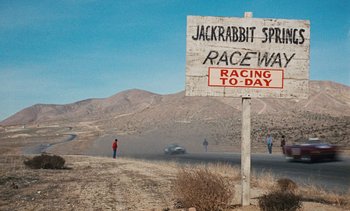 Movie still from “The Love Bug” (1969), directed by Robert Stevenson – A sign that says " racing to - day " on the side of the road; Extreme Wide shot, High angle