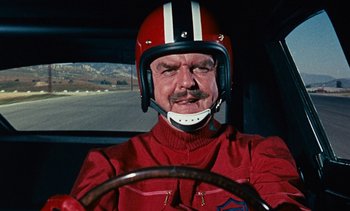 Movie still from “The Love Bug” (1969), directed by Robert Stevenson – A man wearing a helmet driving a car in the road; Close Up shot, Low angle