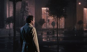 Movie still from “The Love Bug” (1969), directed by Robert Stevenson – A man standing in front of a building with trees; Wide shot, Over the shoulder angle