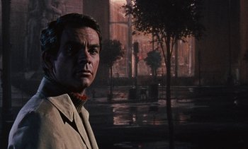 Movie still from “The Love Bug” (1969), directed by Robert Stevenson – A man standing in front of a street with trees; Close Up shot, Low angle