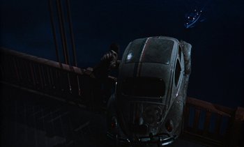 Movie still from “The Love Bug” (1969), directed by Robert Stevenson – A man standing next to an old car on a bridge at night; Wide shot, High angle