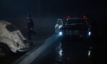 Movie still from “The Love Bug” (1969), directed by Robert Stevenson – A police officer walking near a car in the rain; Wide shot, High angle