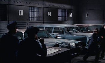 Movie still from “The Love Bug” (1969), directed by Robert Stevenson – A police officer sitting at a desk in front of parked cars; Wide shot, High angle