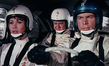 Movie still from “The Love Bug” (1969), directed by Robert Stevenson – A group of men riding in a car on a road; Medium shot, Low angle