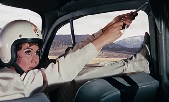 Movie still from “The Love Bug” (1969), directed by Robert Stevenson – A man driving a car while holding a gun; Medium shot, Low angle